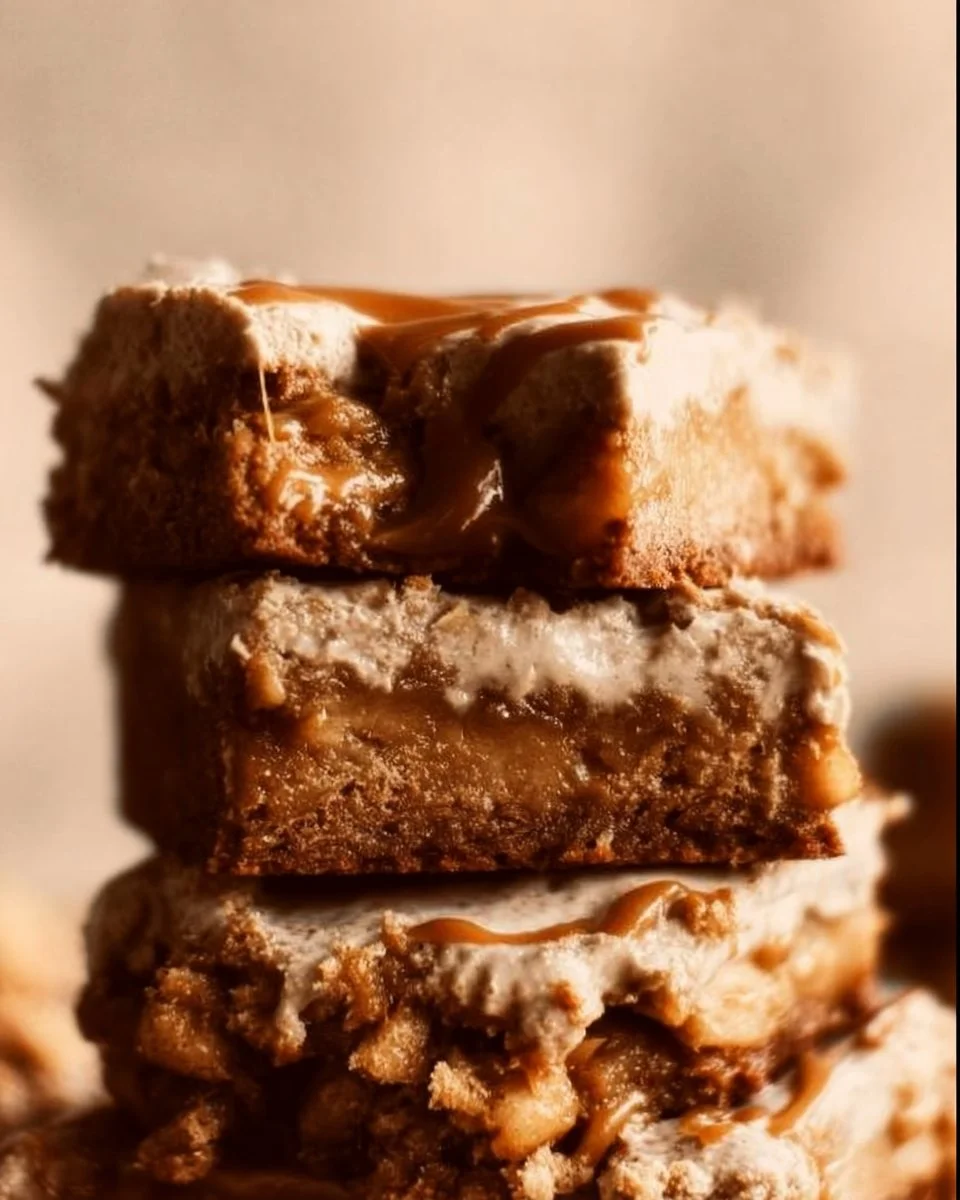 Frosted caramel apple blondies topped with creamy frosting and apple pieces.