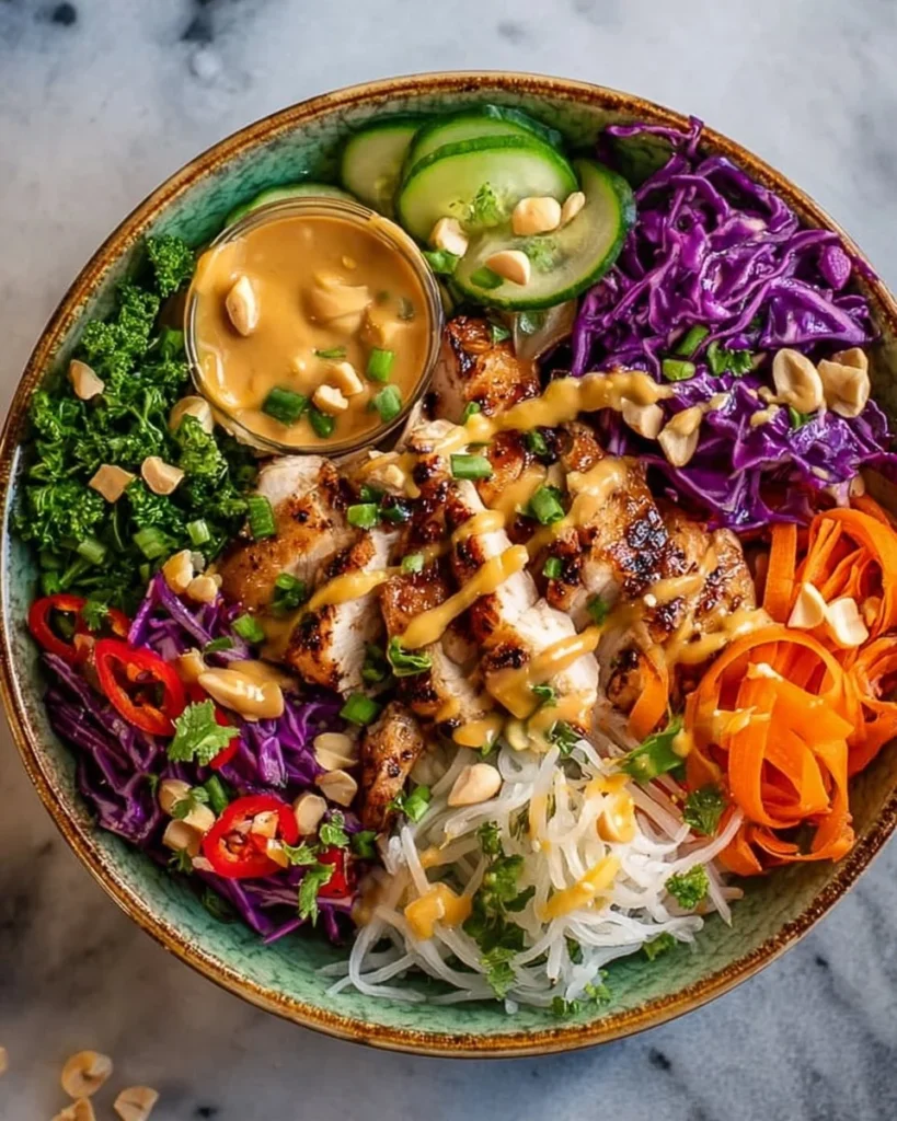 A vibrant Chicken Buddha Bowl topped with peanut sauce, vegetables, and grains.