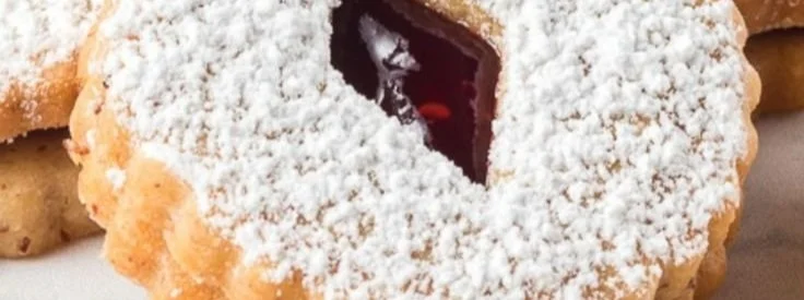 A plate of delicious Linzer Cookies filled with raspberry jam and dusted with powdered sugar.